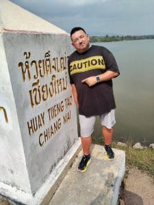 A man pointing at a sign that reads 'Huay Tueng Tai Chiang Mai',