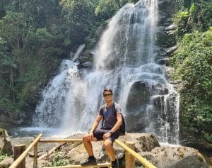 A man posing at the base of a large waterfall