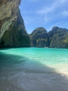 A teal ocean is visible between various hills and mountain formations with trees and plants growing up the sides.