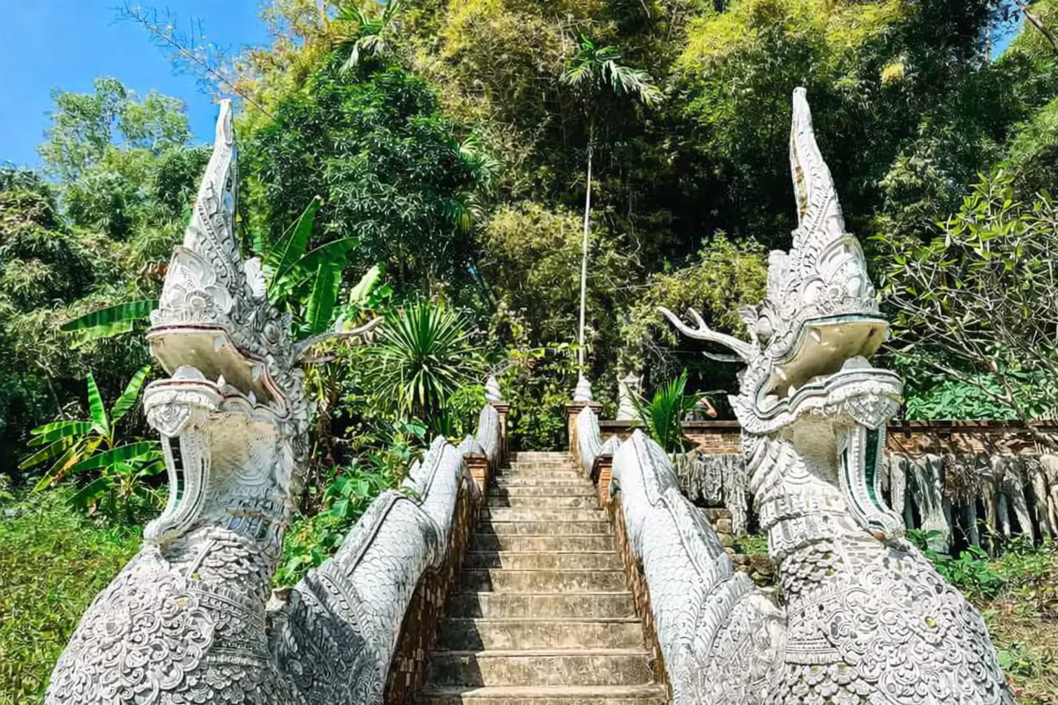A stone stairway, marked at the bottom by two Asian styled dragons leads up into a hill.